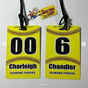 May include: Two yellow softball bag tags with black text and a brown stitched border. One tag has the number "00" and the name "Charleigh" and the other has the number "6" and the name "Chandler". Both tags say "Diamond Thieves". A logo is at the top.
