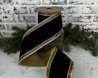May include: A wide spool of black velvet ribbon featuring metallic gold edges and a decorative border of small, dark, reflective beads. The ribbon is wound around a circular core, displaying a smooth, dark texture and a shimmering gold underside.