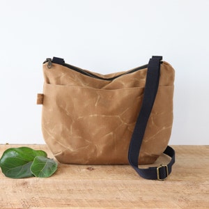 Sac à bandoulière arrondi en toile cirée pour femme et homme, avec fermeture éclair sur le dessus et poche extérieure.Sac robuste en toile cirée pour l'extérieur et les voyages.