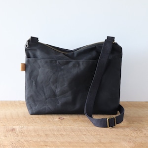 Sac à bandoulière en toile cirée pour femme et homme, avec fermeture éclair sur le dessus et poche extérieure.Sac en toile cirée robuste pour l'extérieur et les voyages.