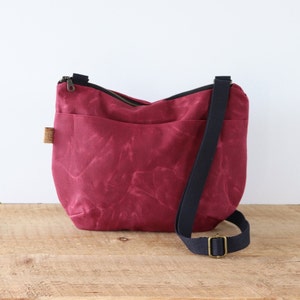 Sac à bandoulière arrondi en toile cirée pour femme et homme, avec fermeture éclair sur le dessus et poche extérieure.Sac robuste en toile cirée pour l'extérieur et les voyages.