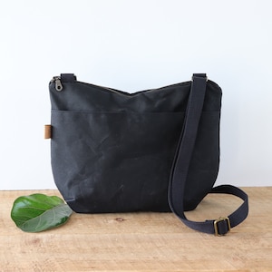 Sac à bandoulière arrondi en toile cirée pour femme et homme, avec fermeture éclair sur le dessus et poche extérieure.Sac robuste en toile cirée pour l'extérieur et les voyages.