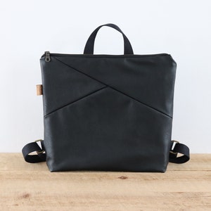 Petit/moyen sac à dos en cuir végétalien pour femme et homme. Sac à main noir chic en similicuir souple, avec fermeture éclair sur le dessus et poches.