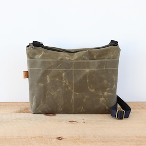 Sac à bandoulière en toile cirée pour femme et homme, avec fermeture éclair sur le dessus et poche extérieure.Sac en toile cirée robuste pour l'extérieur et les voyages.