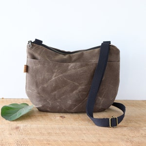 Sac à bandoulière arrondi en toile cirée pour femme et homme, avec fermeture éclair sur le dessus et poche extérieure.Sac robuste en toile cirée pour l'extérieur et les voyages.