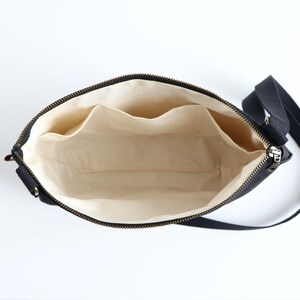 May include: Black canvas crossbody bag with a zipper closure and a beige fabric interior. The bag has two interior pockets.