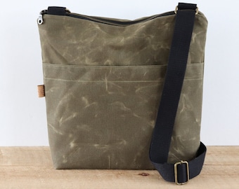 May include: A green canvas crossbody bag with a black adjustable strap and a zipper closure. The bag has a large front pocket.