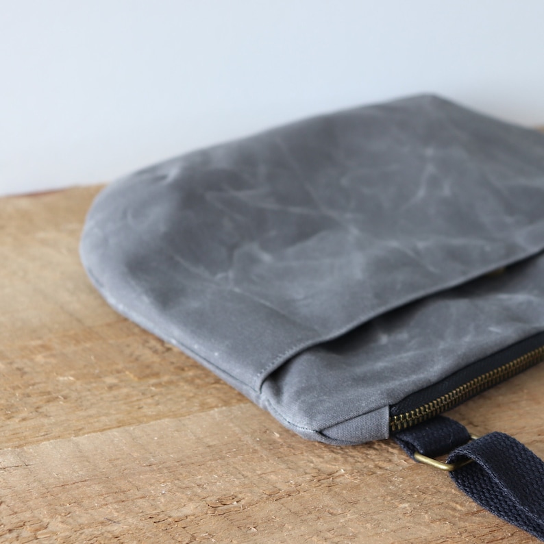 May include: A gray canvas crossbody bag with a zipper closure and a black adjustable strap.