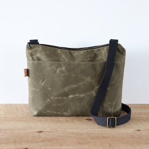Sac à bandoulière en toile cirée pour femme et homme, avec fermeture éclair sur le dessus et poche extérieure.Sac en toile cirée robuste pour l'extérieur et les voyages.