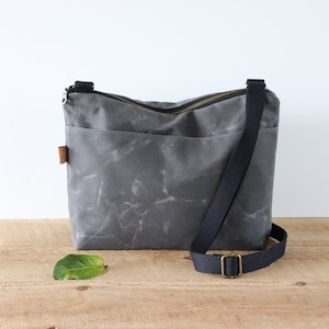 Sac à bandoulière en toile cirée pour femme et homme, avec fermeture éclair sur le dessus et poche extérieure.Sac en toile cirée robuste pour l'extérieur et les voyages.