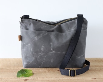 May include: A gray canvas crossbody bag with a zipper closure and a black adjustable strap. The bag has a subtle marbled pattern and a small brown leather patch.