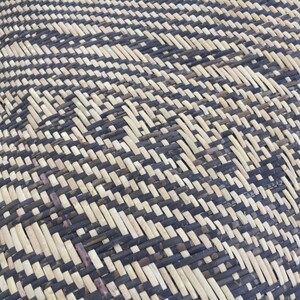 May include: Close-up of a woven basket with a black and natural straw pattern. The basket is made of natural materials and has a unique, intricate design.