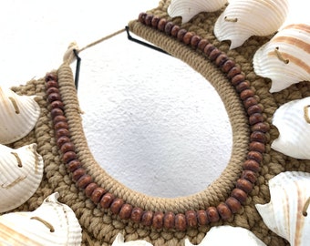 May include: A brown rope necklace with white seashells and brown wooden beads. The necklace is crocheted and has a simple design.