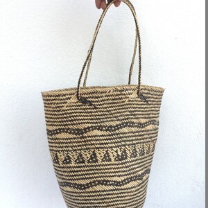 May include: A large, woven tote bag with black and natural brown stripes and a geometric pattern. The bag has two long, woven handles.