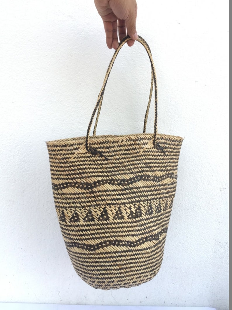 May include: A large, woven tote bag with black and natural brown stripes and a geometric pattern. The bag has two long, woven handles.