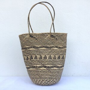 May include: A large, woven tote bag with black and brown geometric patterns. The bag has two thick, woven handles.
