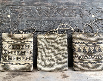 Puede incluir: Tres bolsas de mano tejidas con patrones geométricos en blanco y negro. Las bolsas están hechas de materiales naturales y tienen un aspecto rústico.