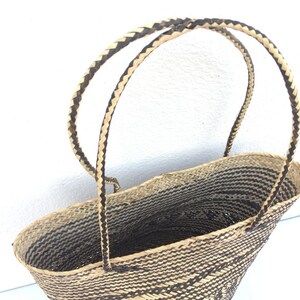 May include: A woven basket with black and natural straw handles. The basket is oval shaped and has a black and natural straw woven pattern.