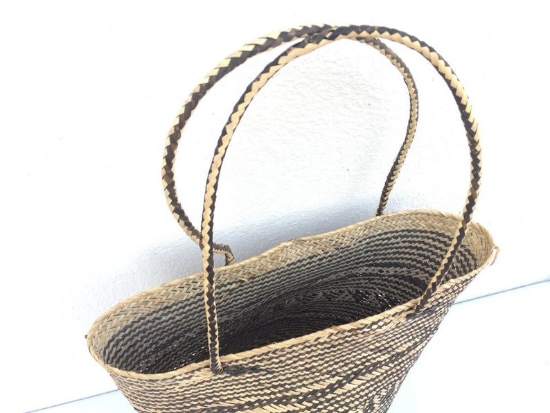 May include: A woven basket with black and natural straw handles. The basket is oval shaped and has a black and natural straw woven pattern.