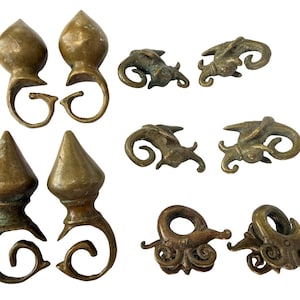 May include: A collection of eight antique brass ornaments featuring various shapes, including four pointed finials with curled bases and four intricate, stylized animal-like figures with curved, swirling details and a weathered, aged metallic patina.