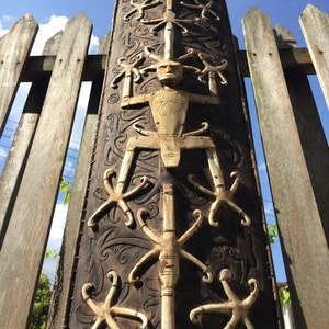May include: A wooden shield with intricate carvings and bone inlays. The shield is decorated with a central figure and a repeating pattern of stylized figures.