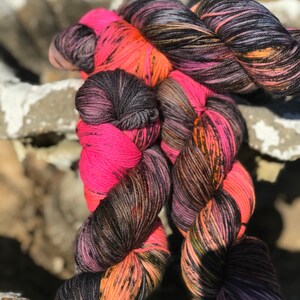 Puede incluir: Tres ovillos de hilo en un esquema de color negro, rosa y naranja. El hilo está retorcido y tiene un aspecto moteado.