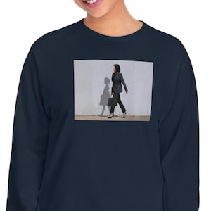 May include: Navy blue long-sleeve shirt featuring a framed image of a person walking in a dark suit. The image is set against a white wall with a shadow. The shirt is a comfortable, casual style.