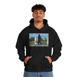 May include: Black hooded sweatshirt with a front graphic. The graphic is a photograph of a person walking in front of the White House. The person is wearing a dark suit and carrying a briefcase.