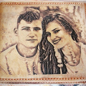 Puede incluir: Una cartera de cuero marr&oacute;n claro con un retrato grabado con l&aacute;ser de una pareja sonriente. La cartera tiene un borde cosido con hilo naranja en contraste. La imagen es un retrato en tonos sepia de un hombre y una mujer.