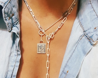 May include: A silver chain necklace with a silver pendant featuring a square design. The pendant has a detailed image of a face and the words "LOVE IS LOVE" inscribed on it.
