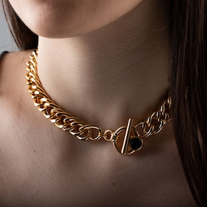 May include: A gold chain necklace with a large, chunky link design. The necklace has a black stone accent on the clasp.