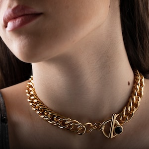 May include: A gold chain choker necklace with a black stone toggle clasp.