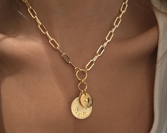 May include: A gold chain necklace with a gold pendant featuring two round medallions. The medallions have a textured surface and are connected by a small gold ring.