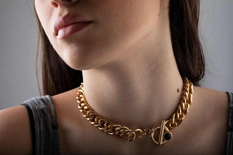 May include: A gold chain choker necklace with a black stone toggle clasp.