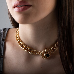 May include: A gold chain necklace with a large, chunky link design. The necklace has a black stone accent on the clasp.