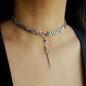 May include: A silver chain choker necklace with a silver sword pendant and a black gemstone.