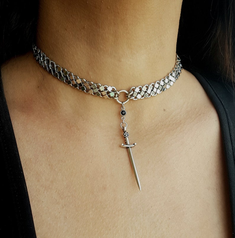 May include: A silver chain choker necklace with a silver sword pendant and a black gemstone.