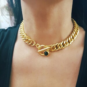 May include: A gold chain necklace with a toggle clasp featuring a black gemstone. The necklace is thick and chunky, with a curb chain design.