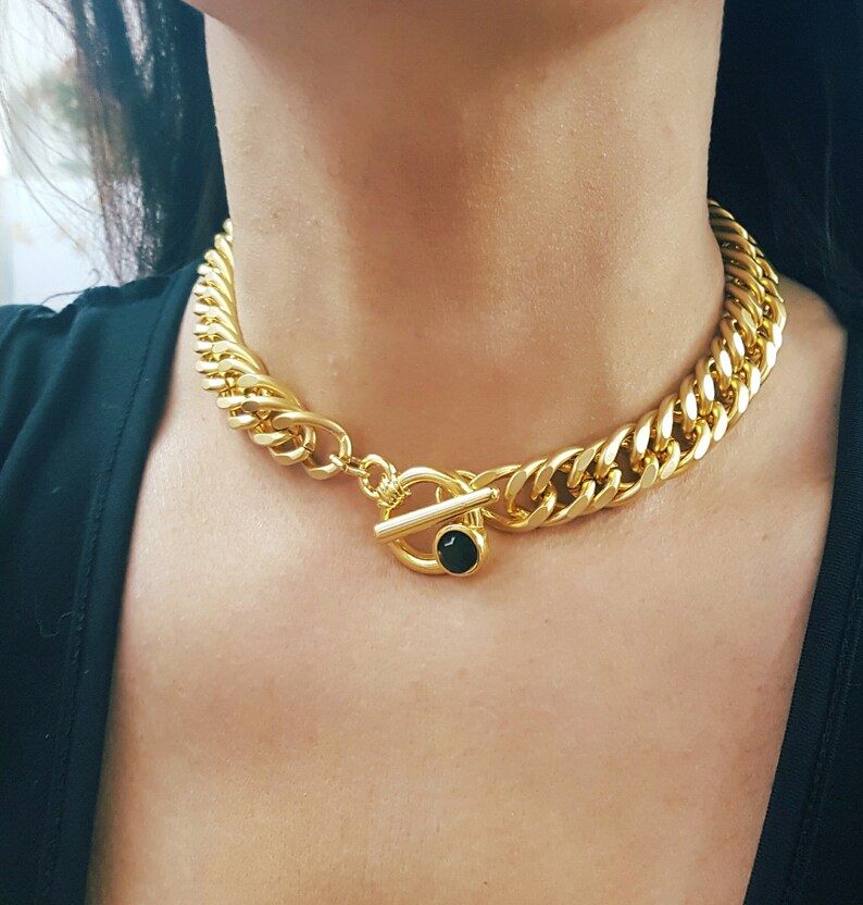 May include: A gold chain necklace with a toggle clasp featuring a black gemstone. The necklace is thick and chunky, with a curb chain design.