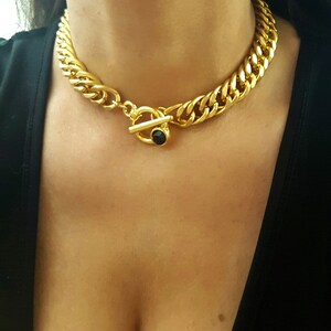 May include: A gold chain necklace with a large, chunky link design. The necklace has a toggle clasp with a black gemstone in the center.
