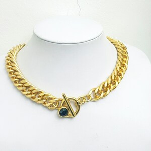 May include: A gold chain necklace with a large, chunky link design. The necklace has a black stone clasp.