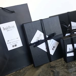 May include: A black gift bag and several black gift boxes tied with black satin ribbon. Each box has a white tag with the text "Bezalel Design" and social media information.