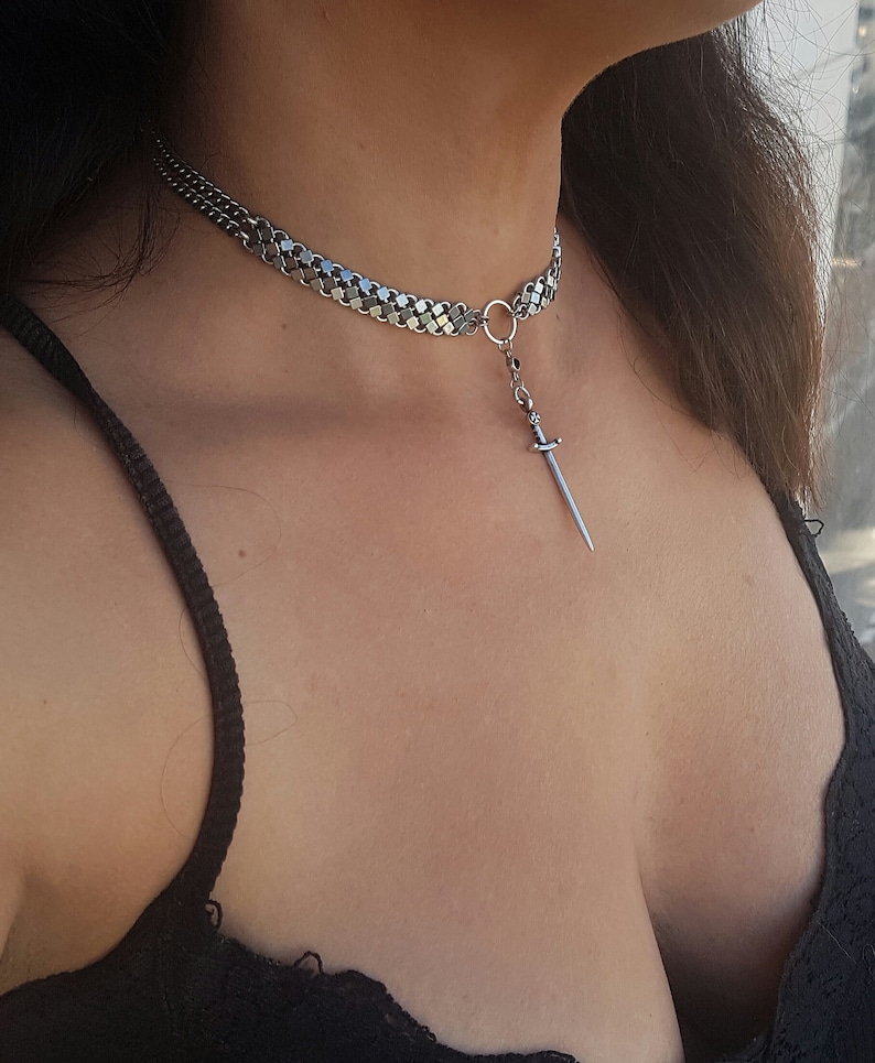 May include: A silver chain choker necklace with a small sword pendant.