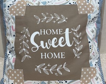 May include: A brown throw pillow with a white floral pattern and the text "Home Sweet Home" in a white script font. The pillow has a brown border and is decorated with beige polka dot fabric accents.