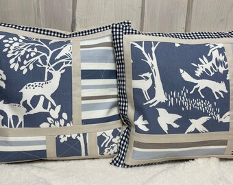 May include: Two blue and white patterned throw pillows with black and white checkered trim. The pillows feature a woodland scene with deer, birds, and trees.