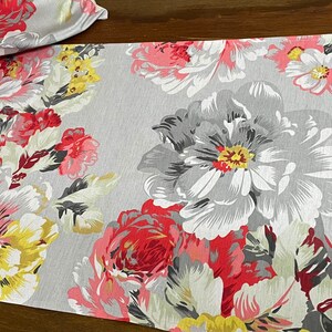 May include: A grey floral table runner with large pink, red, and yellow flowers. The runner has a subtle texture and a modern design.