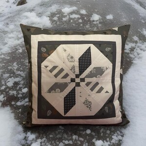Könnte beinhalten: Quadratisches Zierkissen mit Patchwork-Design. Die Mitte zeigt ein geometrisches Sternmuster in Creme, Grau und Schwarz. Der Rand ist dunkelgrau mit einem floralen Muster, und die Kanten sind dunkel olivgrün.
