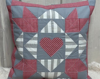 May include: A gray and red patchwork pillow with a heart-shaped design in the center. The pillow is made of gingham and striped fabric.