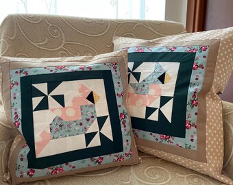 May include: Two decorative throw pillows with a patchwork design featuring a geometric pattern in shades of pink, blue, white, black, and green. The pillows have a brown and white polka dot fabric border.