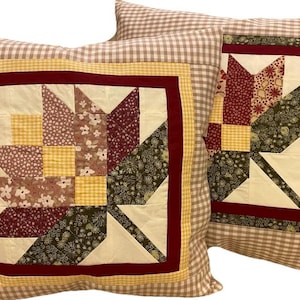 Könnte beinhalten: Zwei dekorative Kissen mit einem karierten Muster und einem Patchwork-Design mit einem Ahornblatt-Motiv in Rot-, Gelb-, Braun- und Grüntönen.